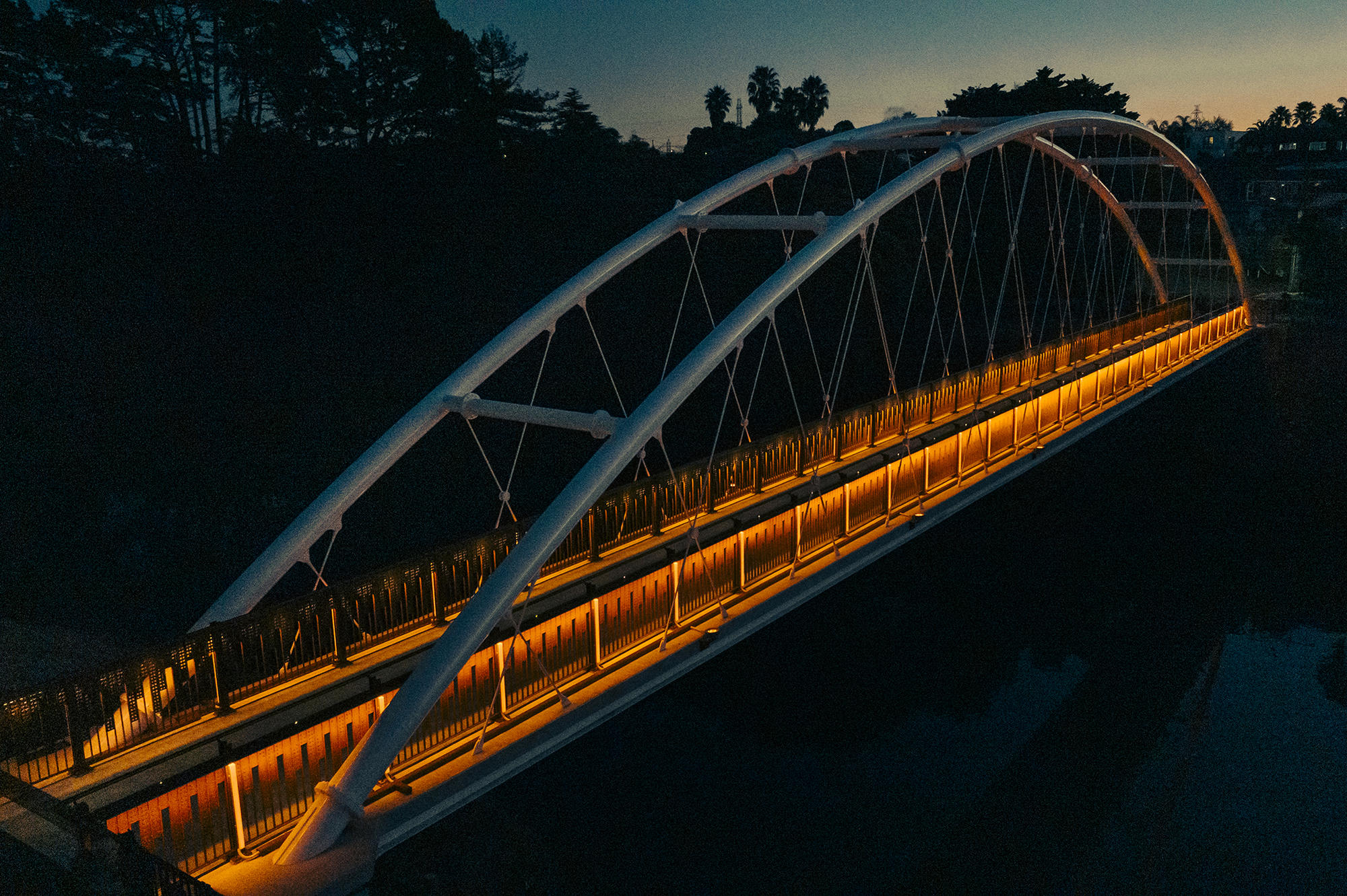 Modern white arch bridge lit with orange lights at night over dark water