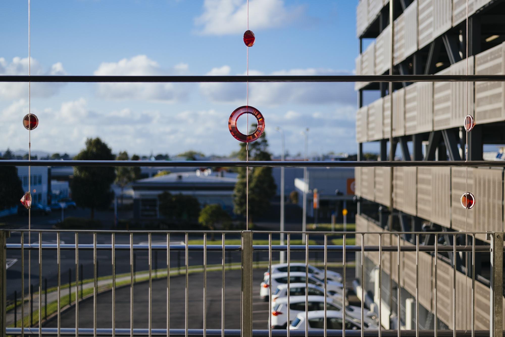 Red glass prisms hanging from wires on a balcony in a parking garage