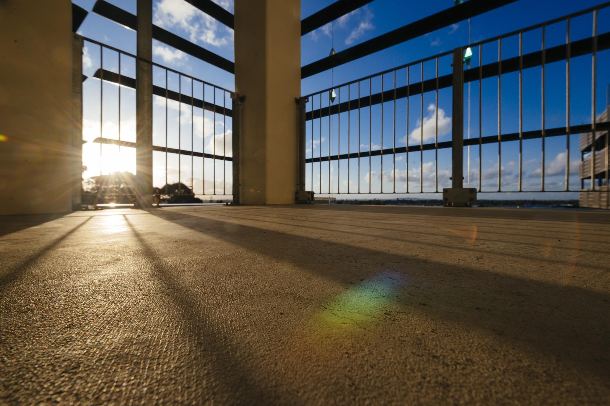 Sunlight streams across a concrete floor and through railings on a balcony, casting rainbows and shadows