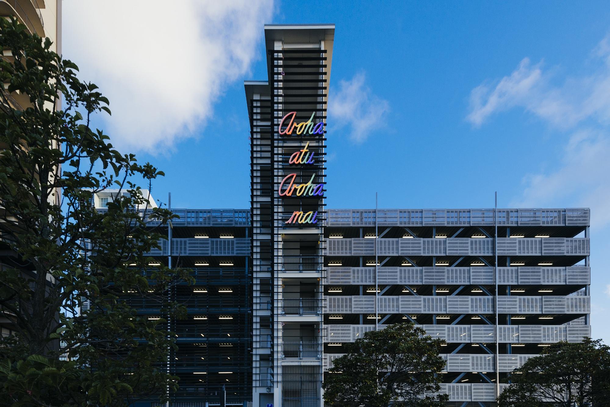 The side of a carpark with a neon sign on the side lit up in rainbow colours