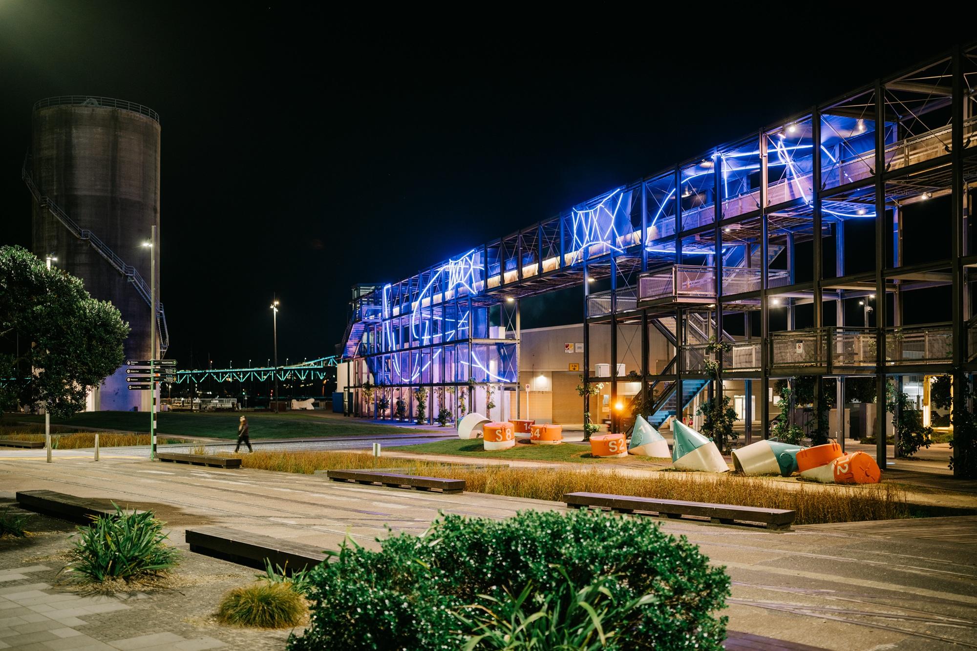An illuminated artwork at night representing whai, te Māori string game, attached to the Gantry at Silo Park