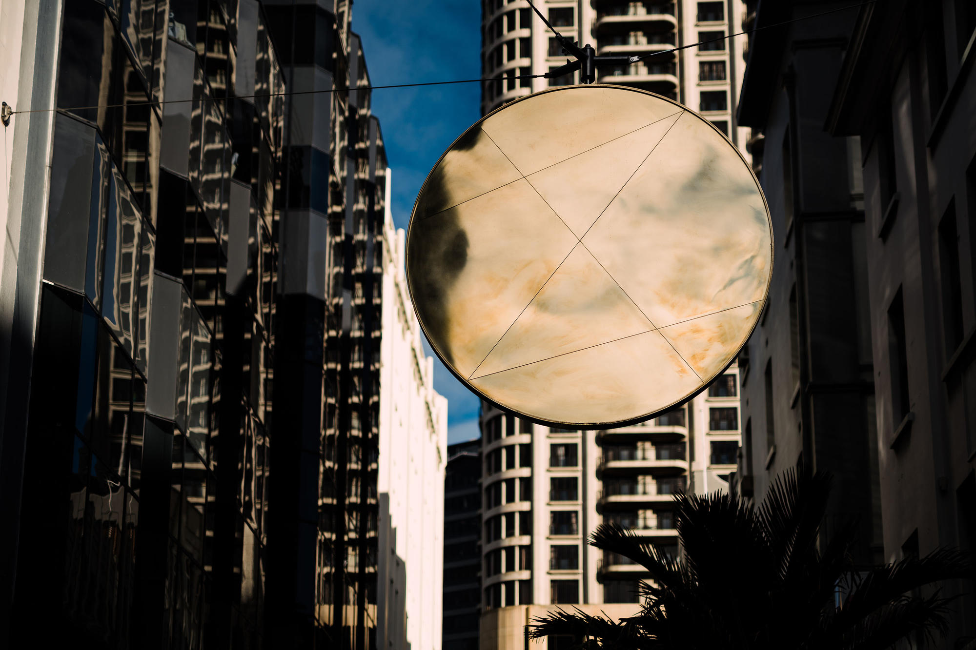 A large round mirror suspended amongst tall buildings reflecting the cloudy sky