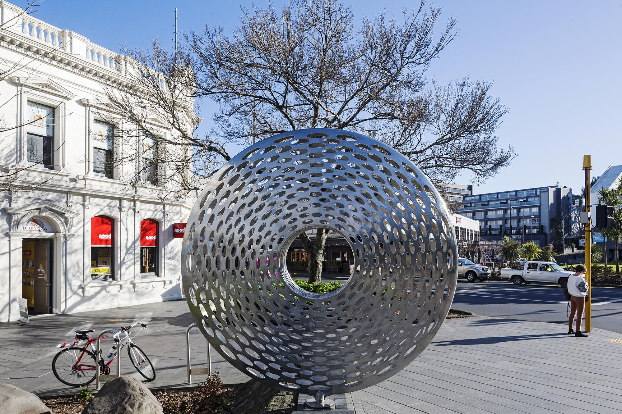 Hollow metal disc sculpture punched with elliptical holes, mounted on paved street corner