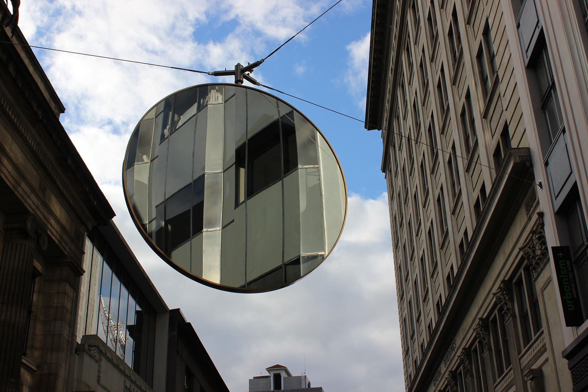 A giant round mirror suspended above O'Connell Street in central Auckland, reflecting the heritage street facade