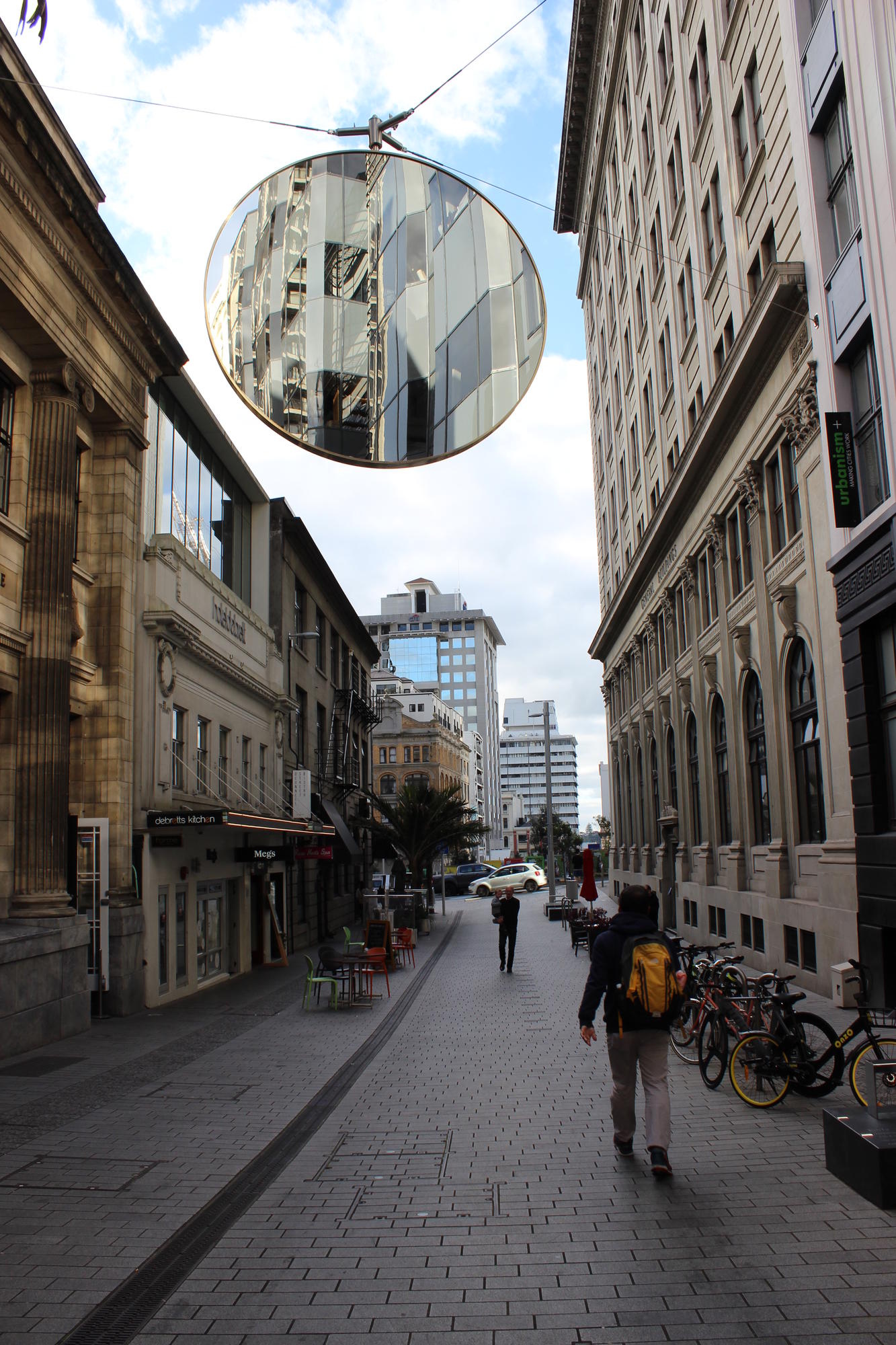 A large round mirror suspended above a narrow lane reflecting the heritage street facade