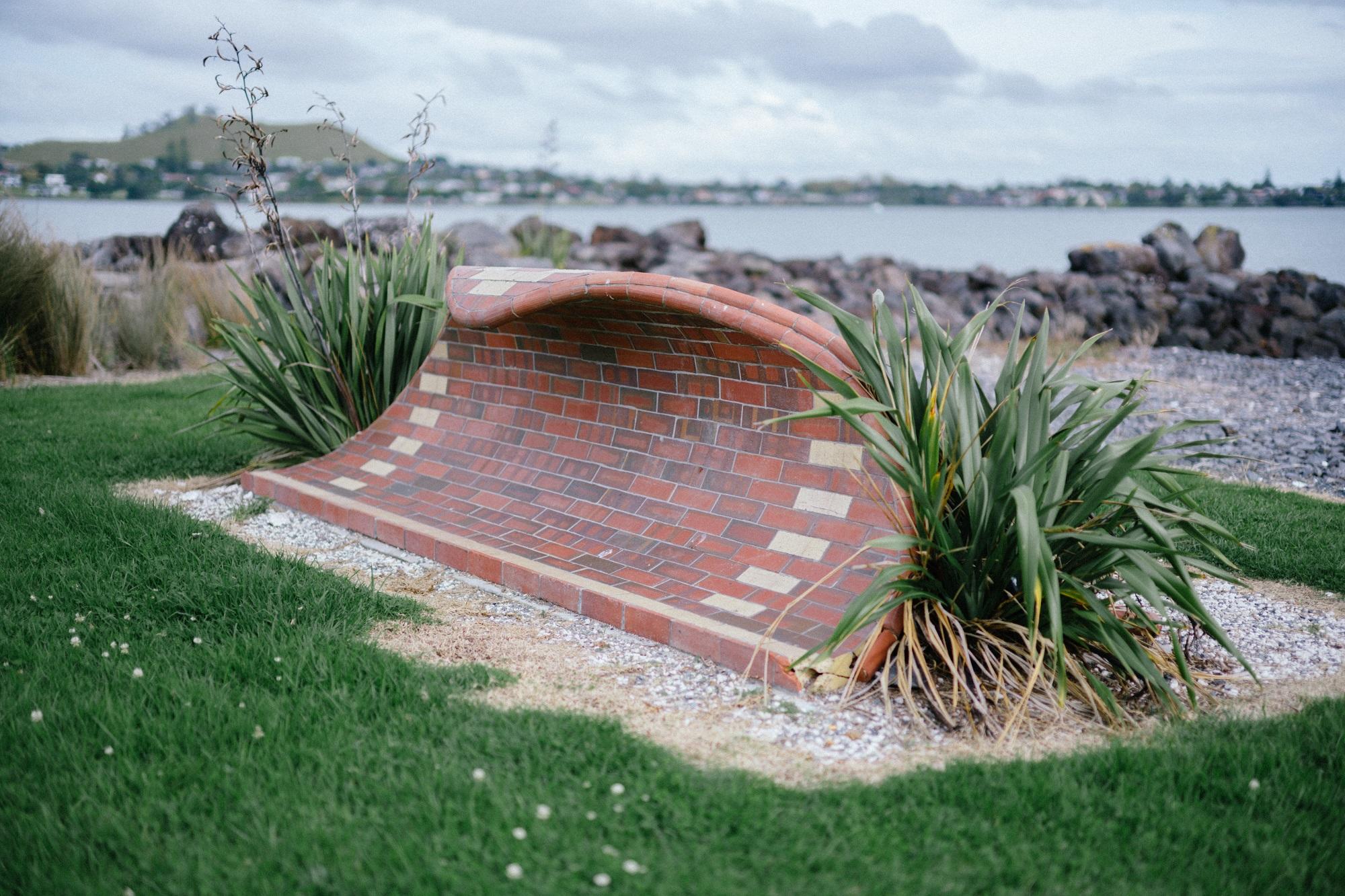 Side view of a brick sculpture with the Manukau Harbour in the background