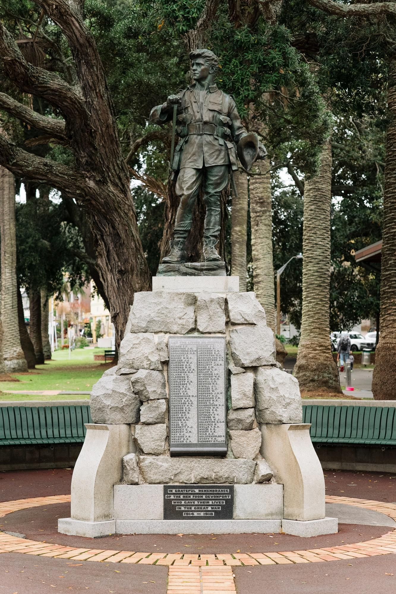 A bronze statue of a soldier stands on a rock plinth with a tree behind