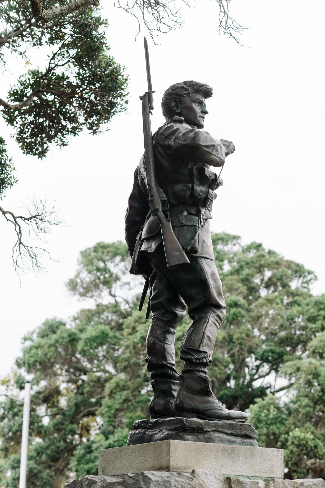 Rear- side view of a bronze soldier statue with gun over one shoulder, standing on a plinth