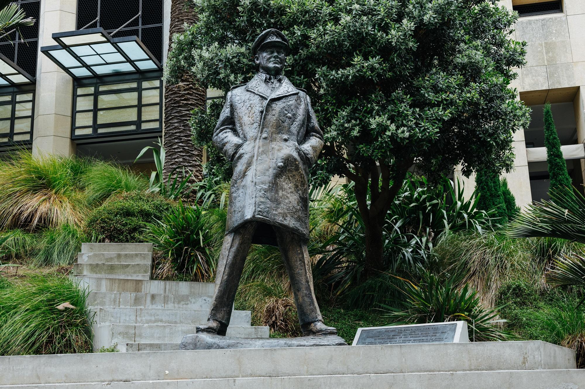A bronze statue of a man wearing a peaked hat and greatcoat standing with his legs apart