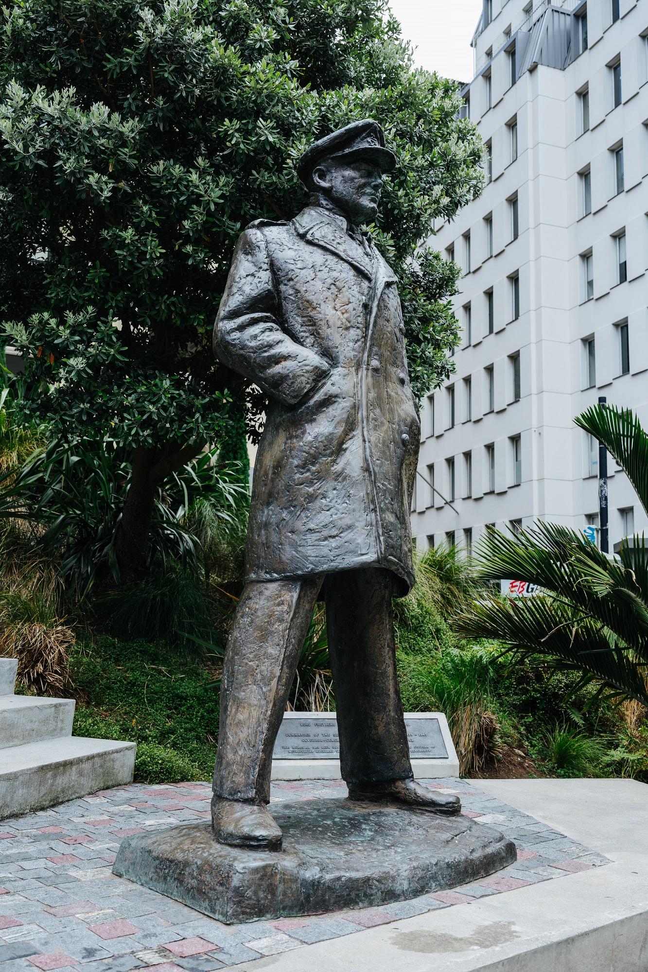 A bronze statue of a man wearing a peaked hat and greatcoat standing with his legs apart