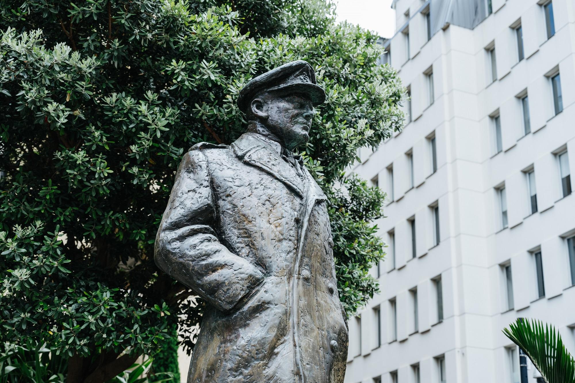 Detail of a bronze statue of a man wearing a peaked hat and greatcoat