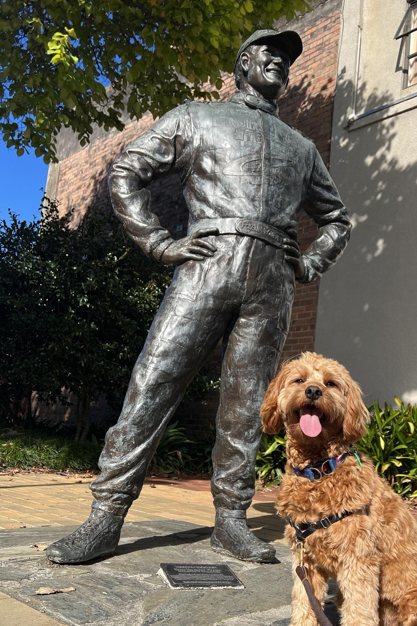 A life size bronze statue of Possum Bourne with a fluffy brown puppy sitting at the base